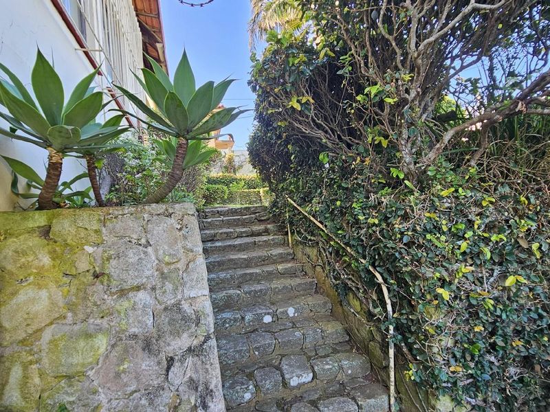 Exterior stone staircase leading up, featuring a rustic stone retaining wall and established garden landscaping with a metal handrail.