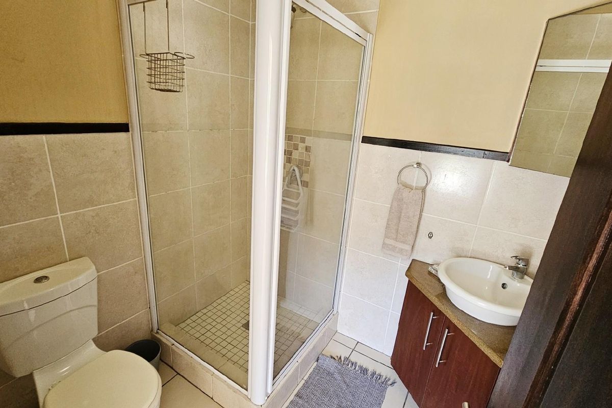 A functional bathroom featuring a corner shower enclosure, a vanity with a basin, and a standard toilet with neutral wall tiling.