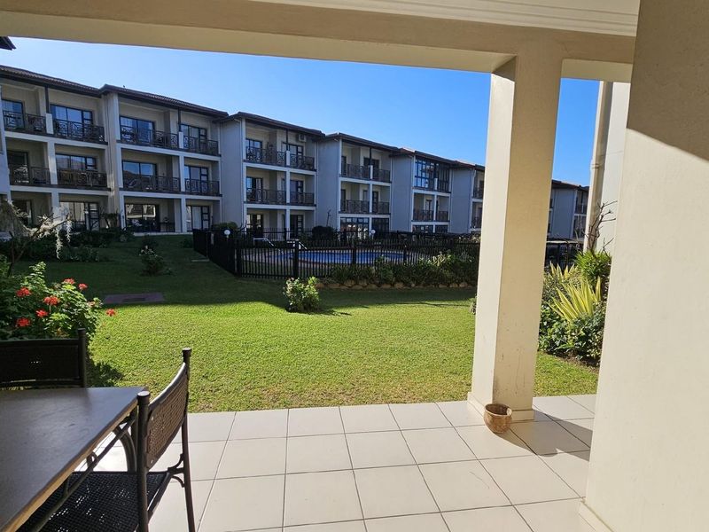A covered patio overlooking a well-maintained communal garden and swimming pool area within an apartment complex.