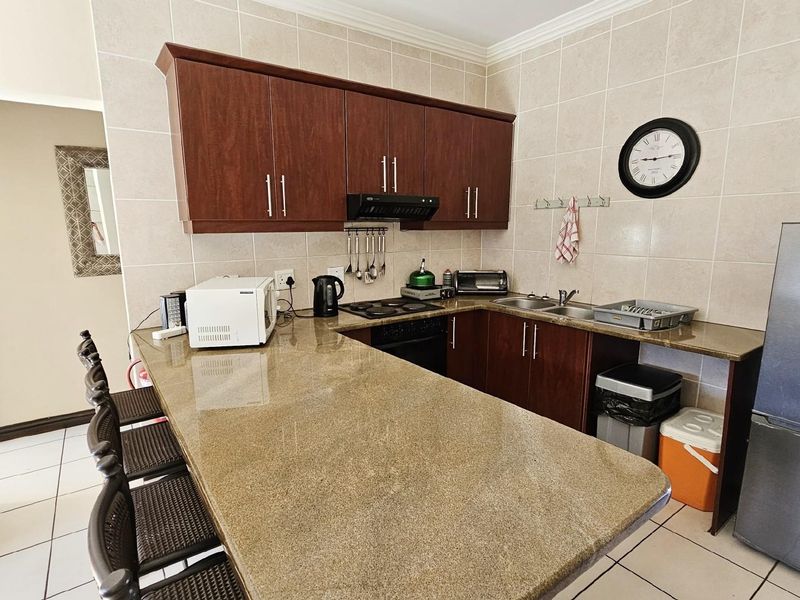 A functional kitchen featuring granite countertops, dark wood cabinetry, a built-in hob, extractor fan, and a double sink with tiled splashbacks.