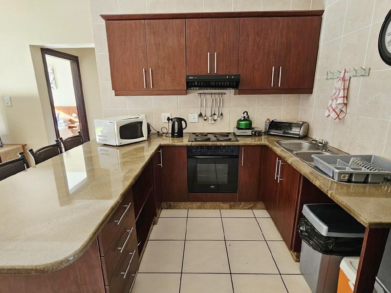 A functional U-shaped kitchen featuring dark wood cabinetry, granite countertops, a built-in oven, and a ceramic hob with an extractor fan.