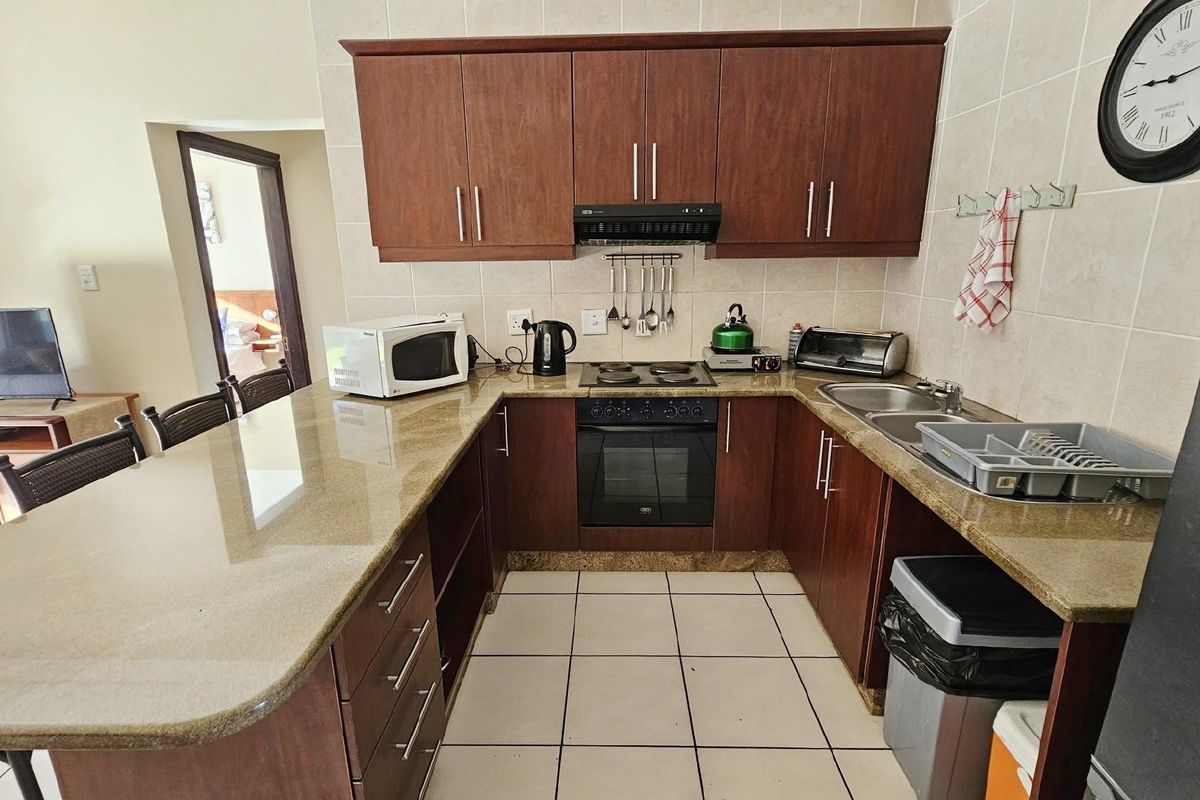 A functional U-shaped kitchen featuring dark wood cabinetry, granite countertops, a built-in oven, and a ceramic hob with an extractor fan.