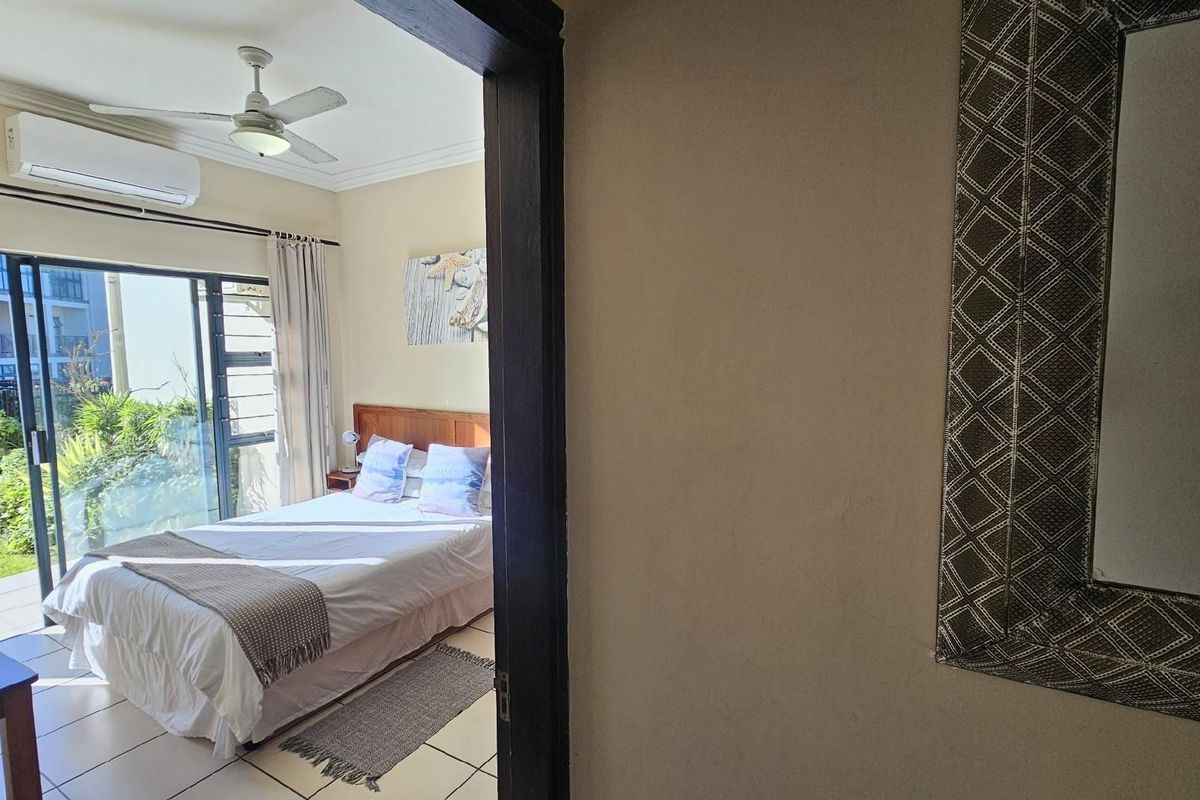 A bright bedroom featuring tiled flooring, a ceiling fan, and a wall-mounted air conditioning unit, with sliding glass doors leading to an outdoor area.