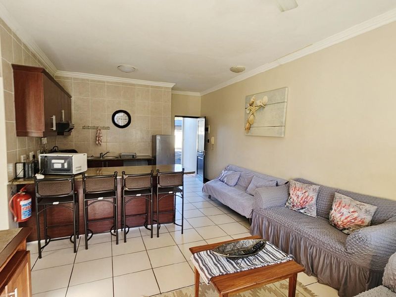 Open-plan living area featuring a kitchen with built-in cabinetry, tiled backsplash, and a breakfast bar counter, seamlessly flowing into the lounge space.