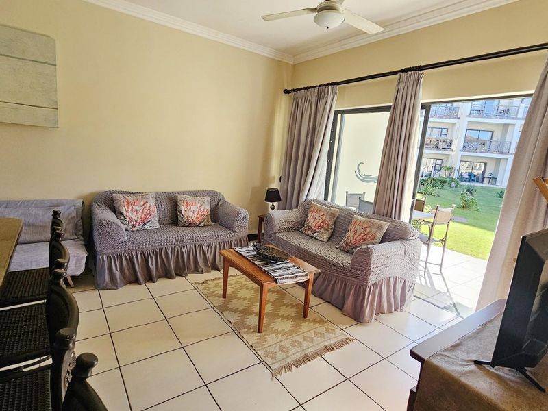 Open plan living area featuring tiled flooring, ceiling fan, and large sliding glass doors providing direct access to the patio and garden.