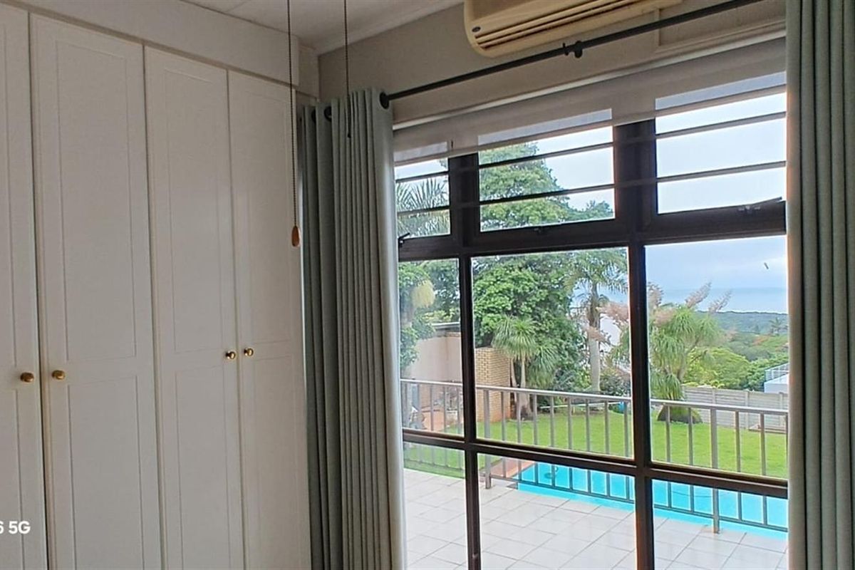 A bedroom featuring built-in white cabinetry and a large window with views overlooking the garden and swimming pool area.