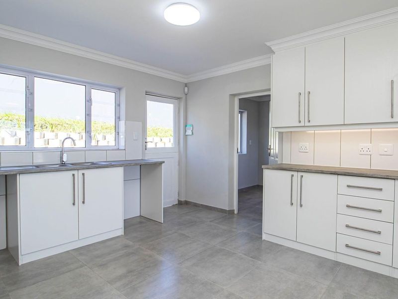 A clean, modern kitchen featuring white cabinetry, grey tiled flooring, laminate countertops, and a stainless steel sink with a window view.