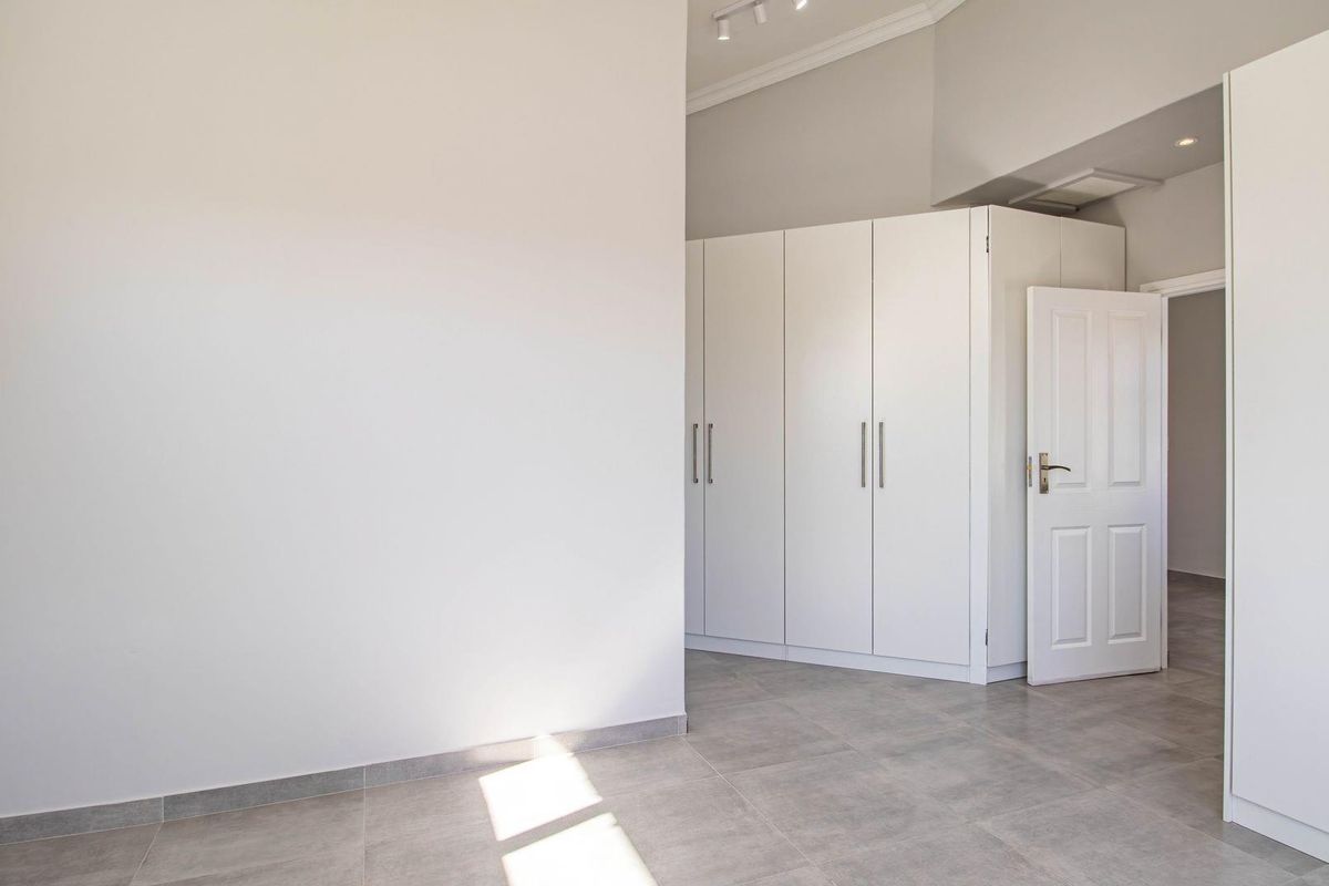 A bright, empty bedroom featuring neutral floor tiles, built-in white cabinetry, and a clean, modern aesthetic.
