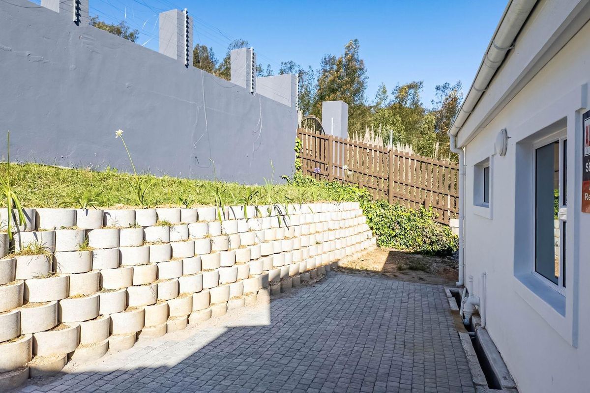 Side exterior area featuring a paved walkway, concrete block retaining wall, and perimeter security fencing with an electric fence system.