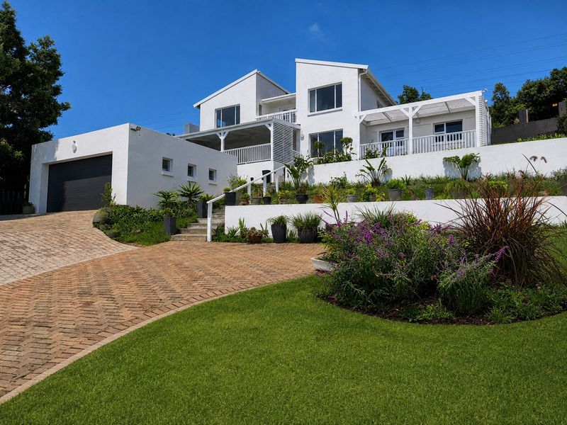 Modern multi-level white house featuring a paved driveway, double garage, terraced garden, and elevated balconies with pergola structures.