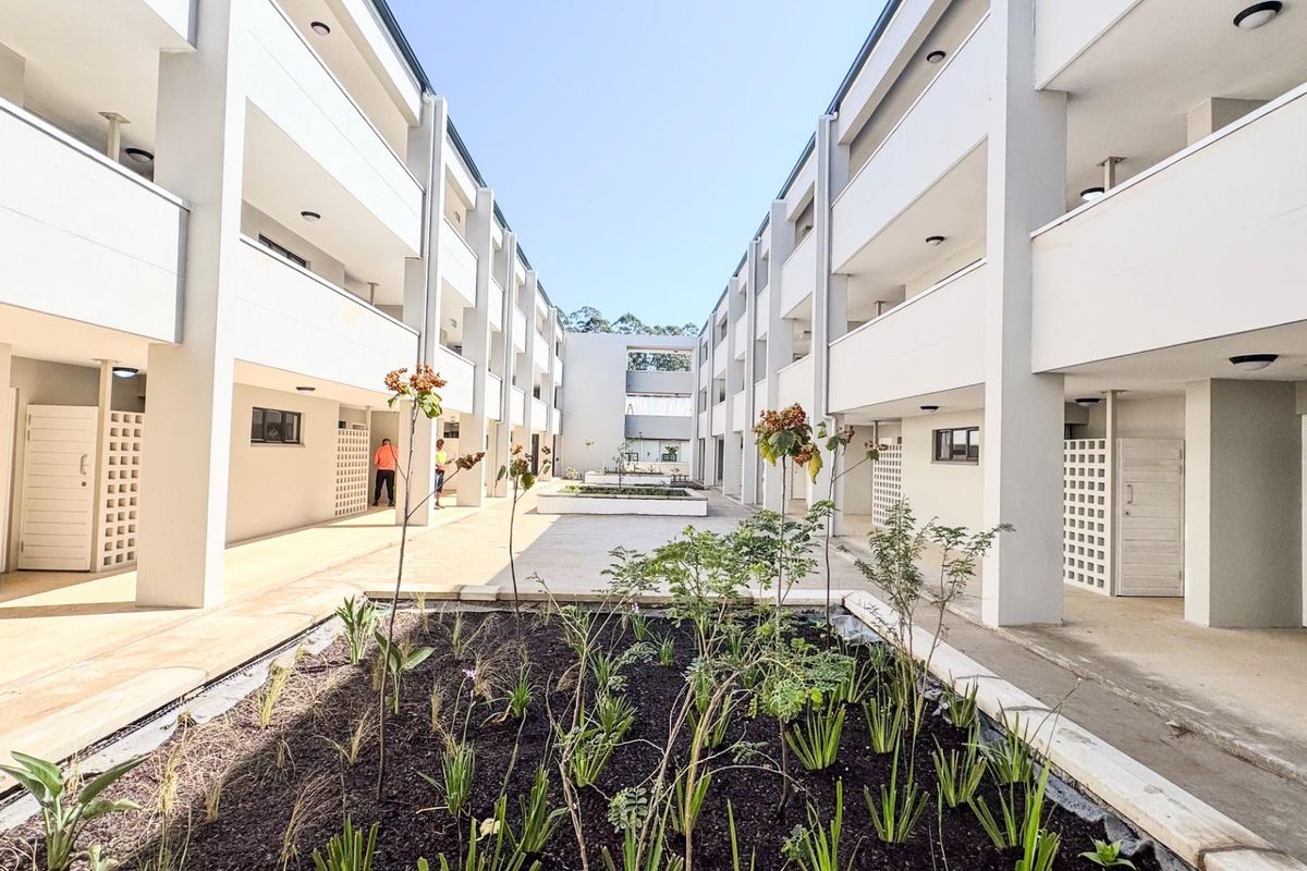 A well-maintained apartment complex courtyard featuring landscaped garden beds, paved walkways, and multi-level balcony access.