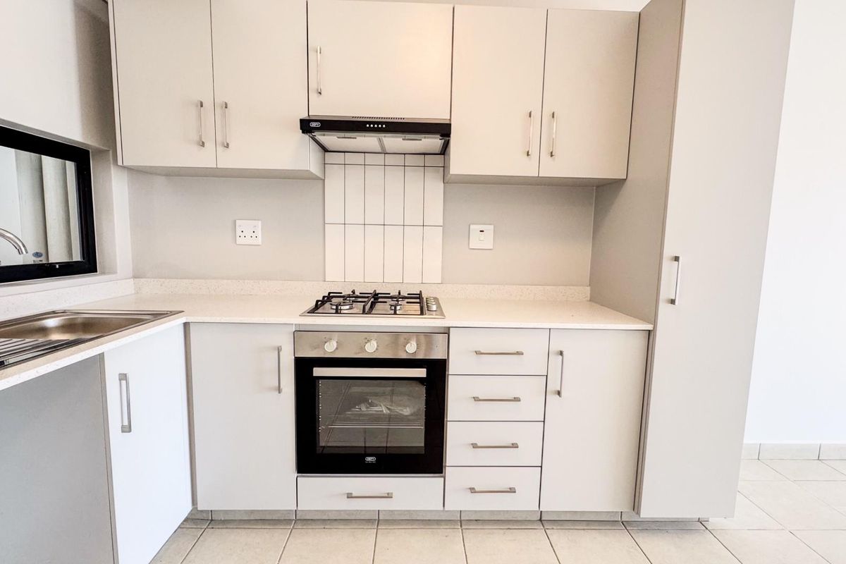Modern kitchen featuring neutral cabinetry, built-in gas hob, oven, extractor fan, and stainless steel sink with tiled flooring.