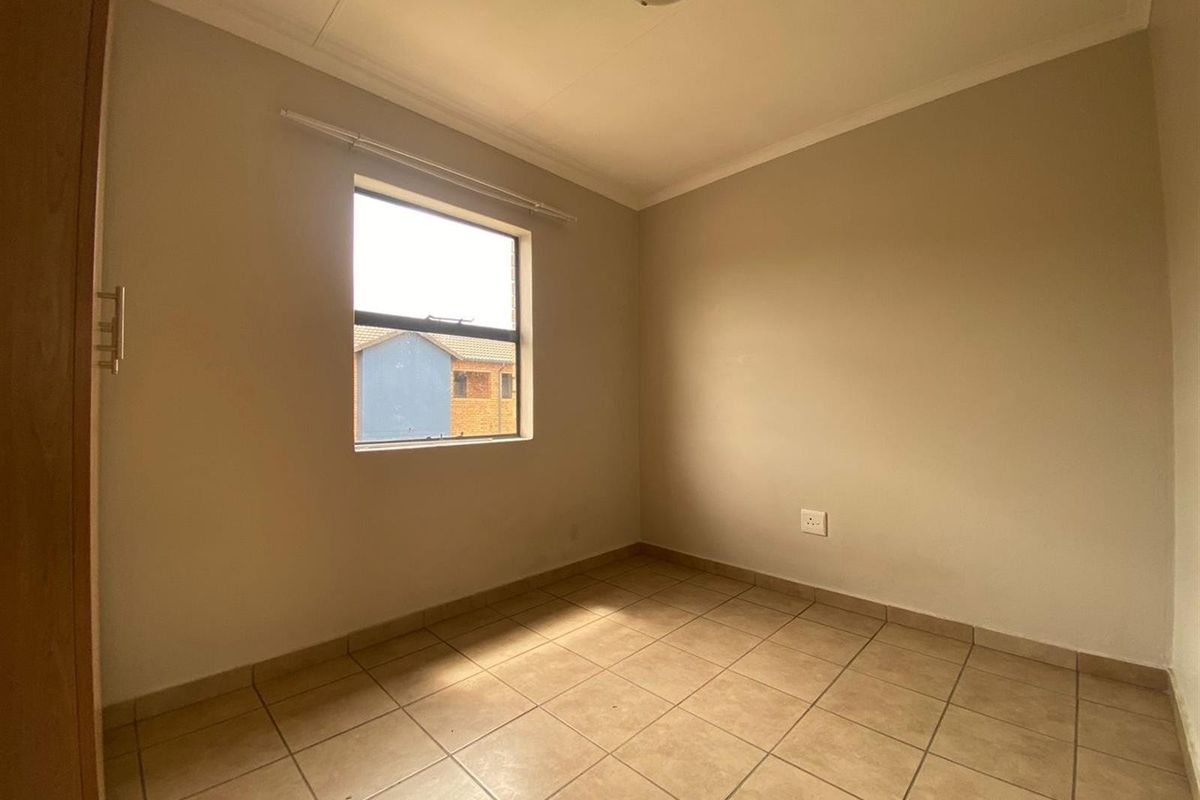A clean, empty bedroom featuring neutral tiled flooring, a built-in cupboard, and a window providing natural light.