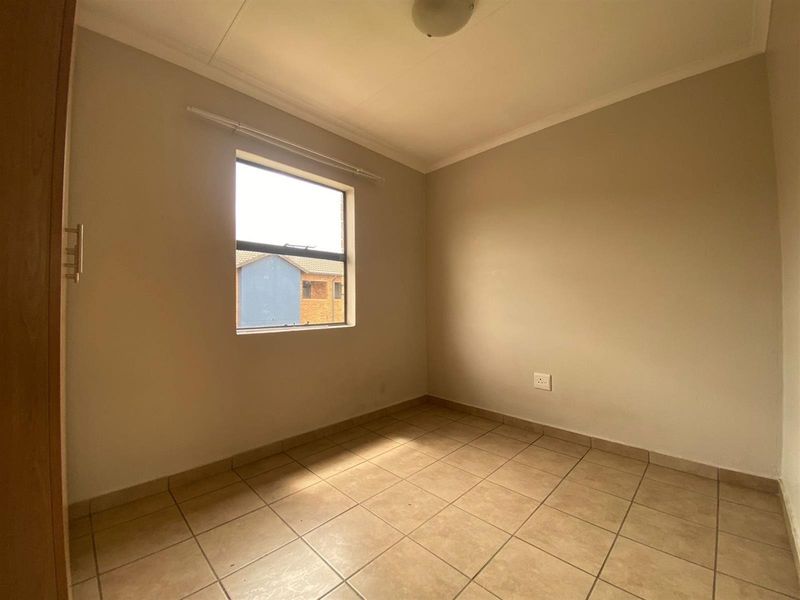 A clean, empty bedroom featuring neutral tiled flooring, a built-in cupboard, and a window providing natural light.