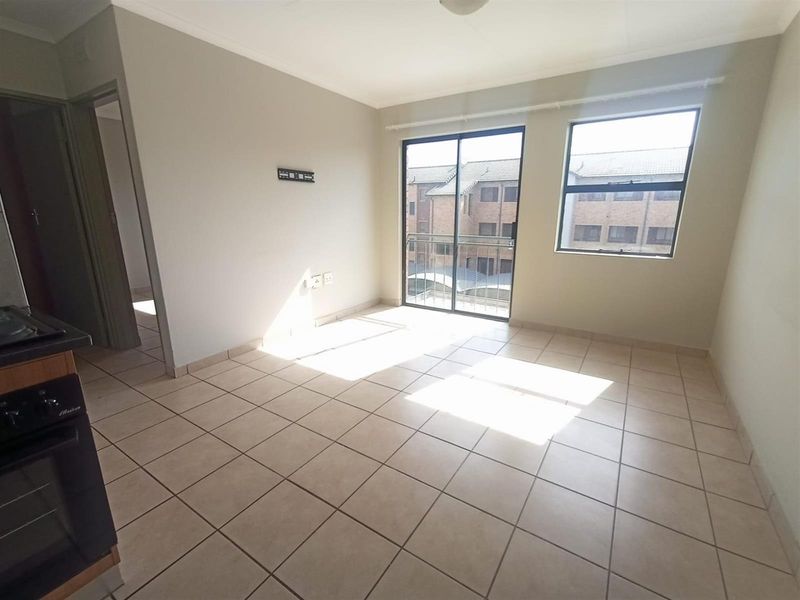 An open-plan living and kitchen area featuring tiled flooring, a built-in oven, and a sliding glass door leading to a balcony.