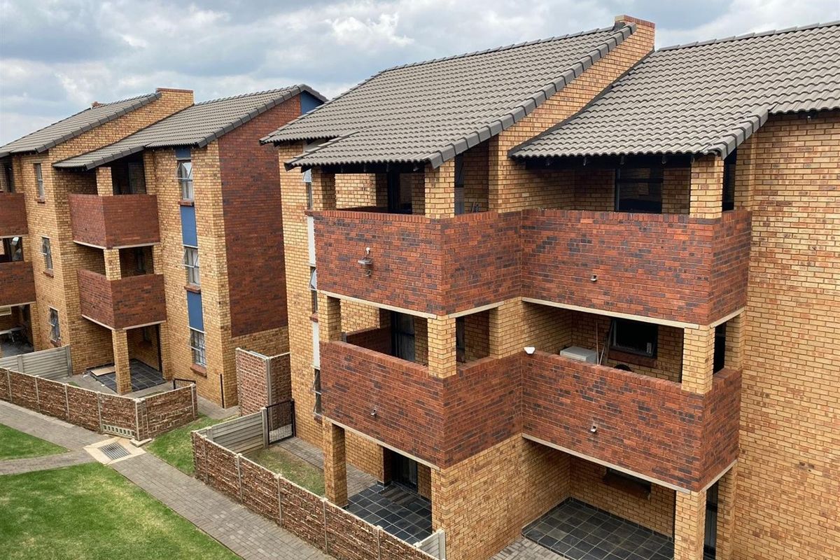 Exterior view of a multi-story apartment complex featuring face brick facades, tiled roofing, and private balconies overlooking a landscaped garden area.