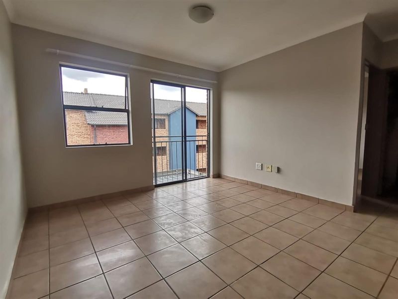 An empty, neutrally painted living area featuring tiled flooring, a sliding glass door leading to a balcony, and functional electrical points.