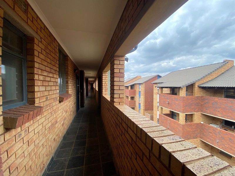 An open-air apartment complex hallway featuring exposed brickwork and tiled flooring, providing access to residential units.