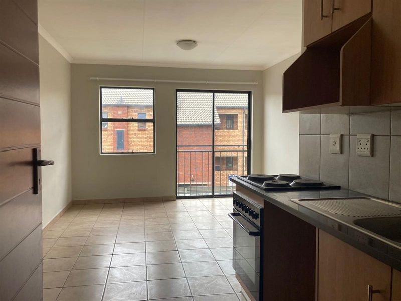 Open-plan living area featuring tiled floors, a functional kitchen with built-in stove and oven, and access to a balcony through sliding doors.