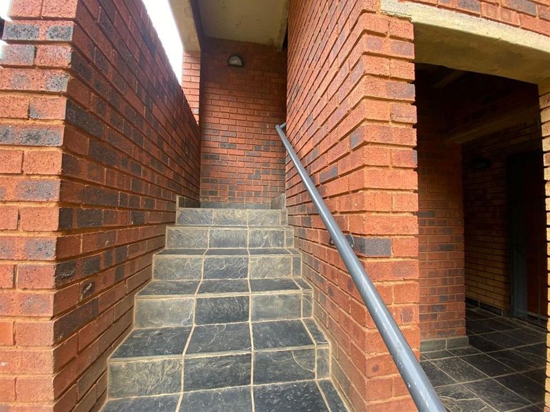 Exterior entrance featuring a face brick staircase with tiled steps and a metal handrail leading to the apartment entry.