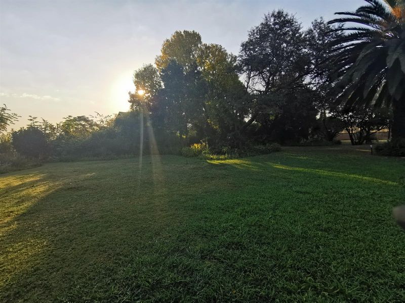A spacious, well-maintained garden area on the small holding, featuring mature trees and expansive lawn space under soft sunset lighting.