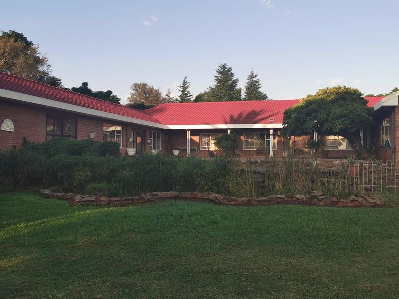 A view of the rear exterior of the small holding, featuring a red tiled roof, brick facade, and a landscaped garden with a pond.