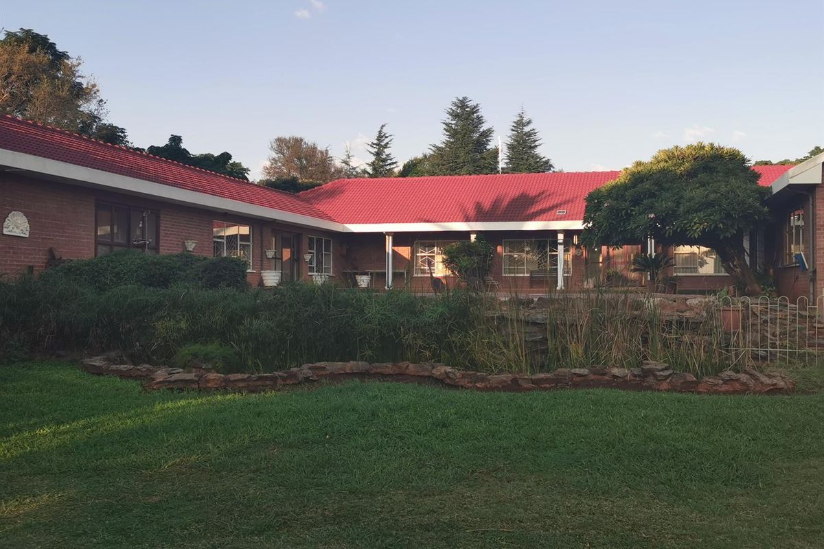A view of the rear exterior of the small holding, featuring a red tiled roof, brick facade, and a landscaped garden with a pond.
