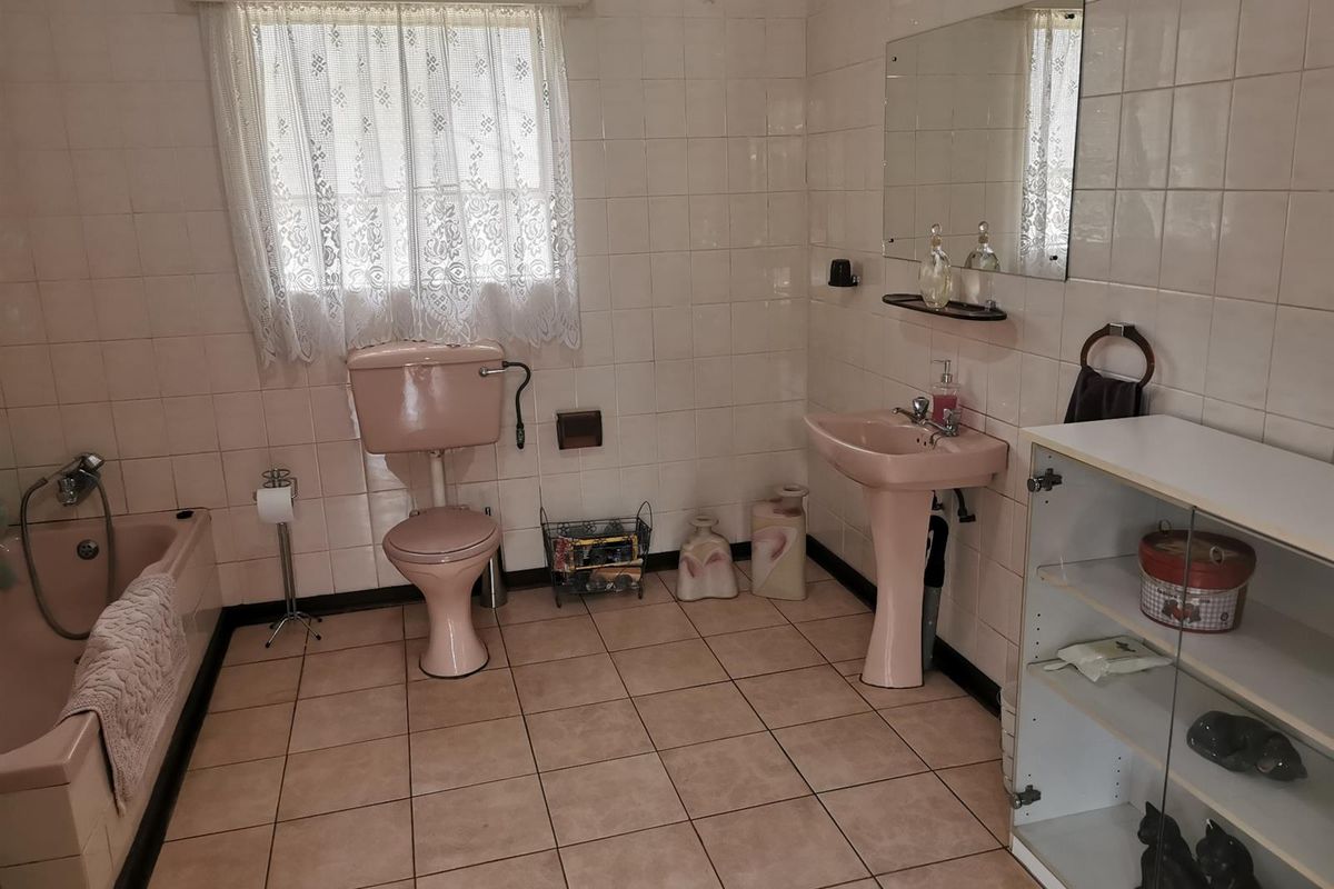 A dated bathroom featuring a vintage pink bathtub, pedestal basin, and toilet, complemented by full-height wall tiling and ceramic floor tiles.