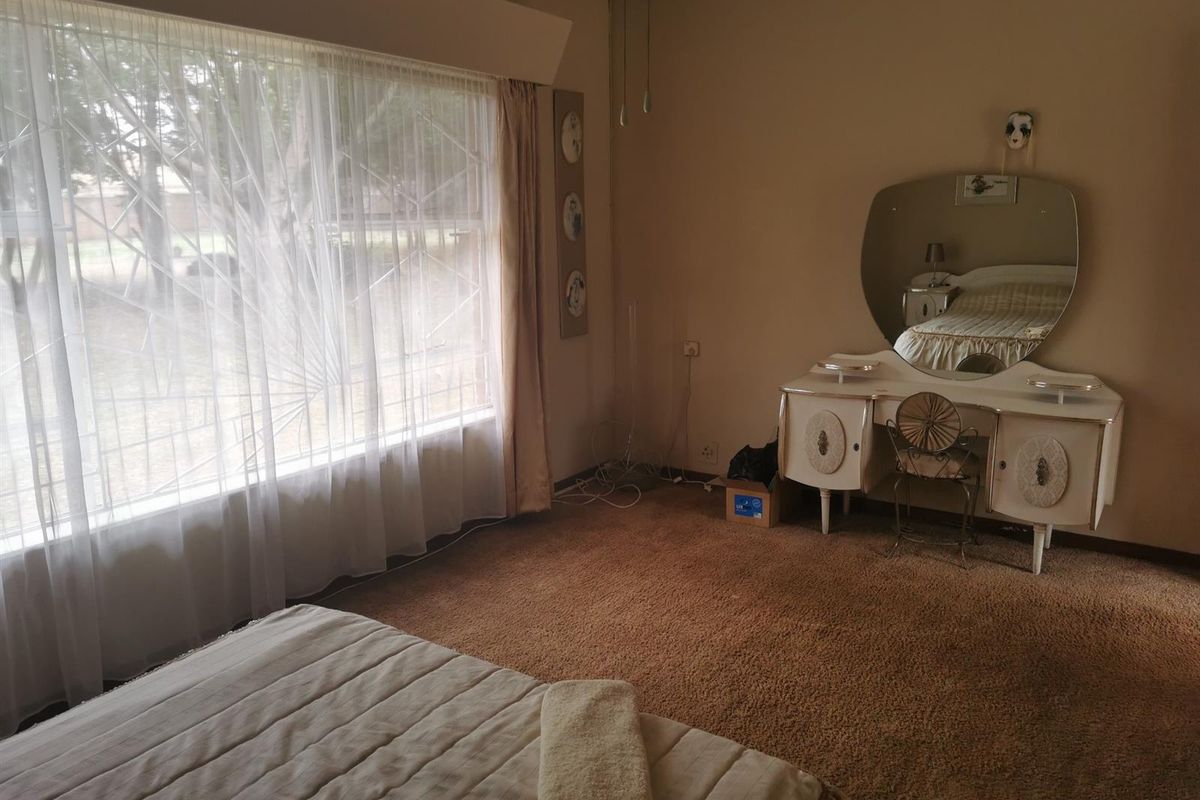A spacious bedroom featuring large windows with natural light, neutral wall tones, and fitted carpeting.