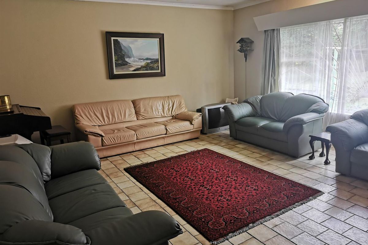 A spacious living room featuring tiled flooring, a ceiling fan, and large windows that provide natural light.