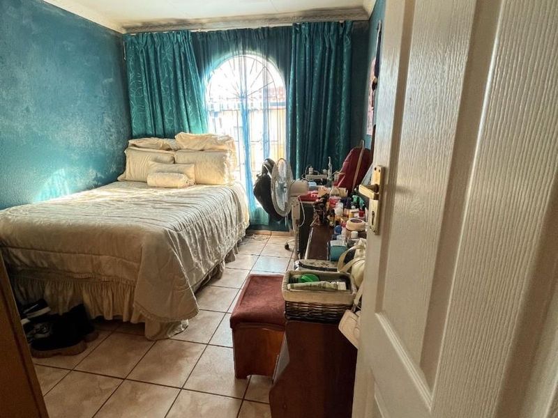 A bedroom featuring tiled flooring, an arched window with security bars, and decorative ceiling cornicing, currently requiring cosmetic updates to the wall finishes.