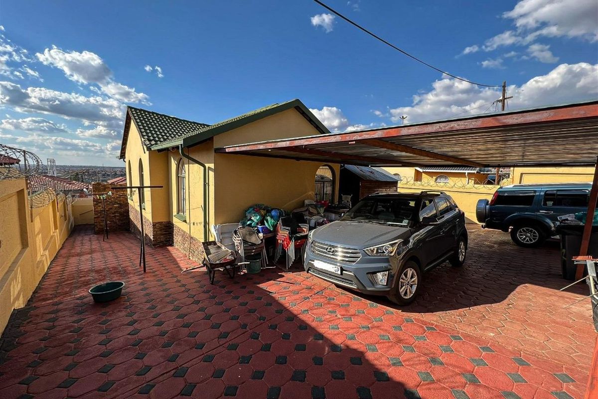 Rear exterior view of the property featuring a paved driveway, a covered carport, and perimeter walling with security fencing.