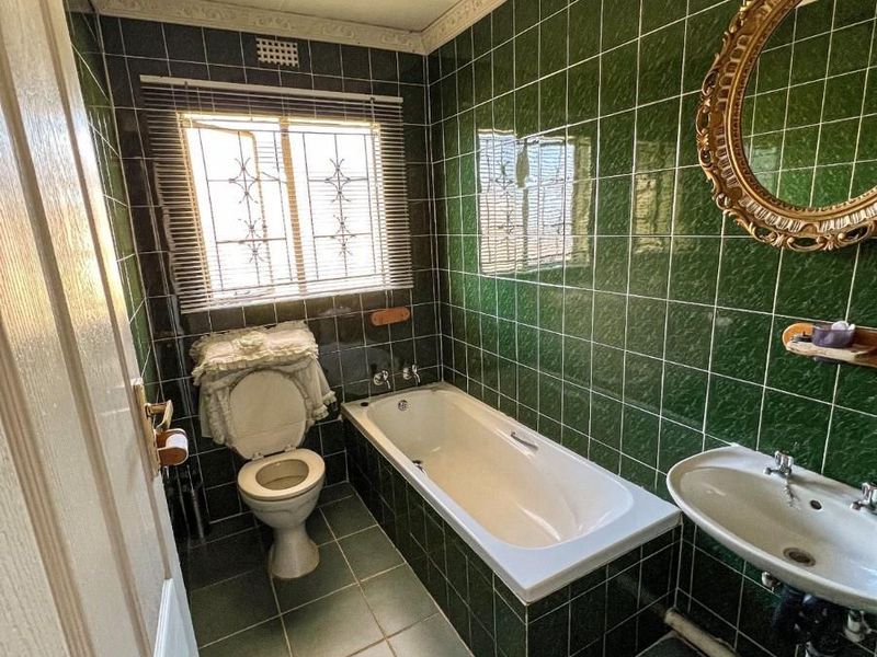 A dated bathroom featuring dark green wall and floor tiles, a built-in bathtub, pedestal sink, and toilet with decorative ceiling cornice.