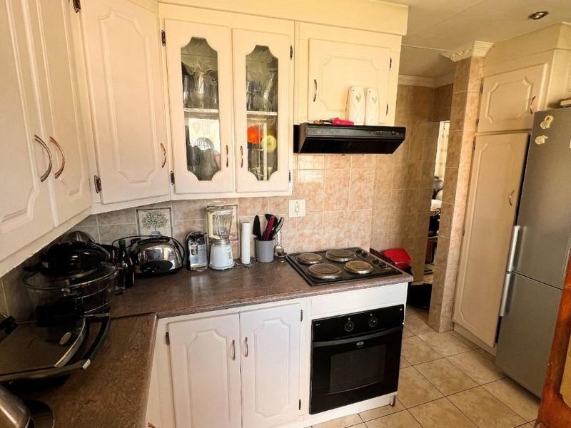 A functional kitchen featuring white cabinetry, laminate countertops, built-in oven and hob, and tiled flooring, offering a classic layout with potential for modernization.