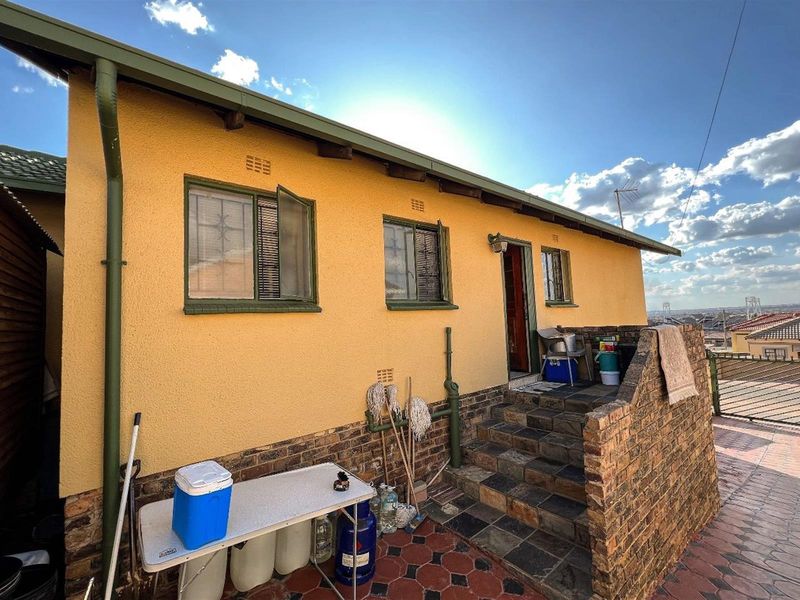 Rear exterior view of the house featuring a brick staircase, paved patio area, and yellow textured wall finish.