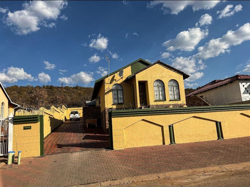Front view of a detached house featuring a paved driveway, perimeter wall with security fencing, and arched windows under a tiled roof.