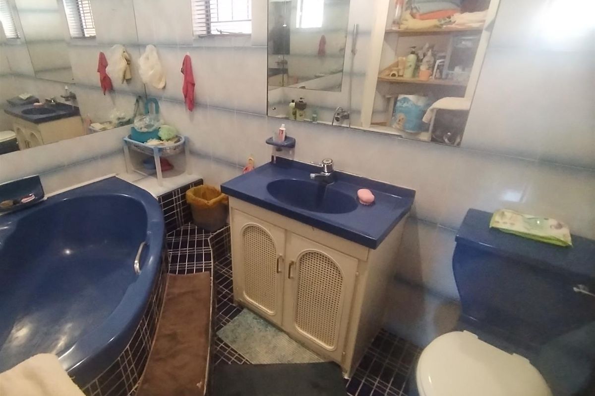 A dated bathroom featuring a blue bathtub, matching blue toilet, and a vanity cabinet with integrated sink and wall-to-wall mirror.