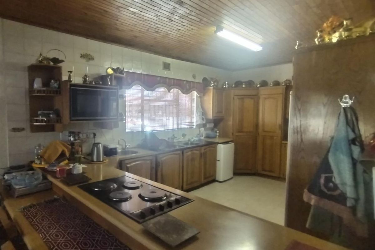 A dated kitchen featuring wooden cabinetry, a built-in electric hob, and a timber-paneled ceiling, offering a functional layout with ample storage space.