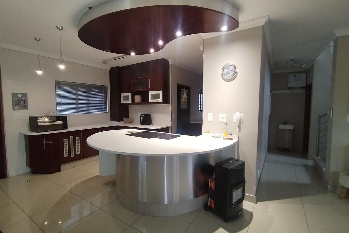 Modern kitchen featuring a curved breakfast bar, dark wood cabinetry, integrated cooktop, and a distinctive circular bulkhead ceiling feature with recessed lighting.