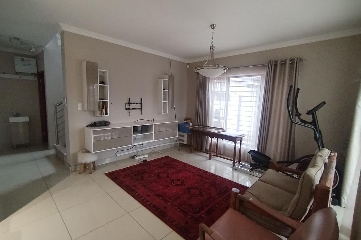 A spacious living room featuring tiled flooring, built-in wall cabinetry, and large windows with curtains, providing a functional and well-lit living area.