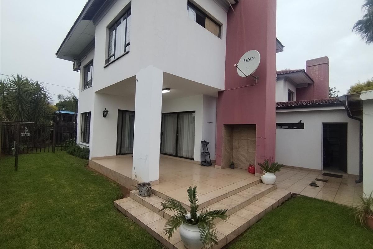 A rear view of a two-story house featuring a covered tiled patio, built-in fireplace, and a spacious garden area.
