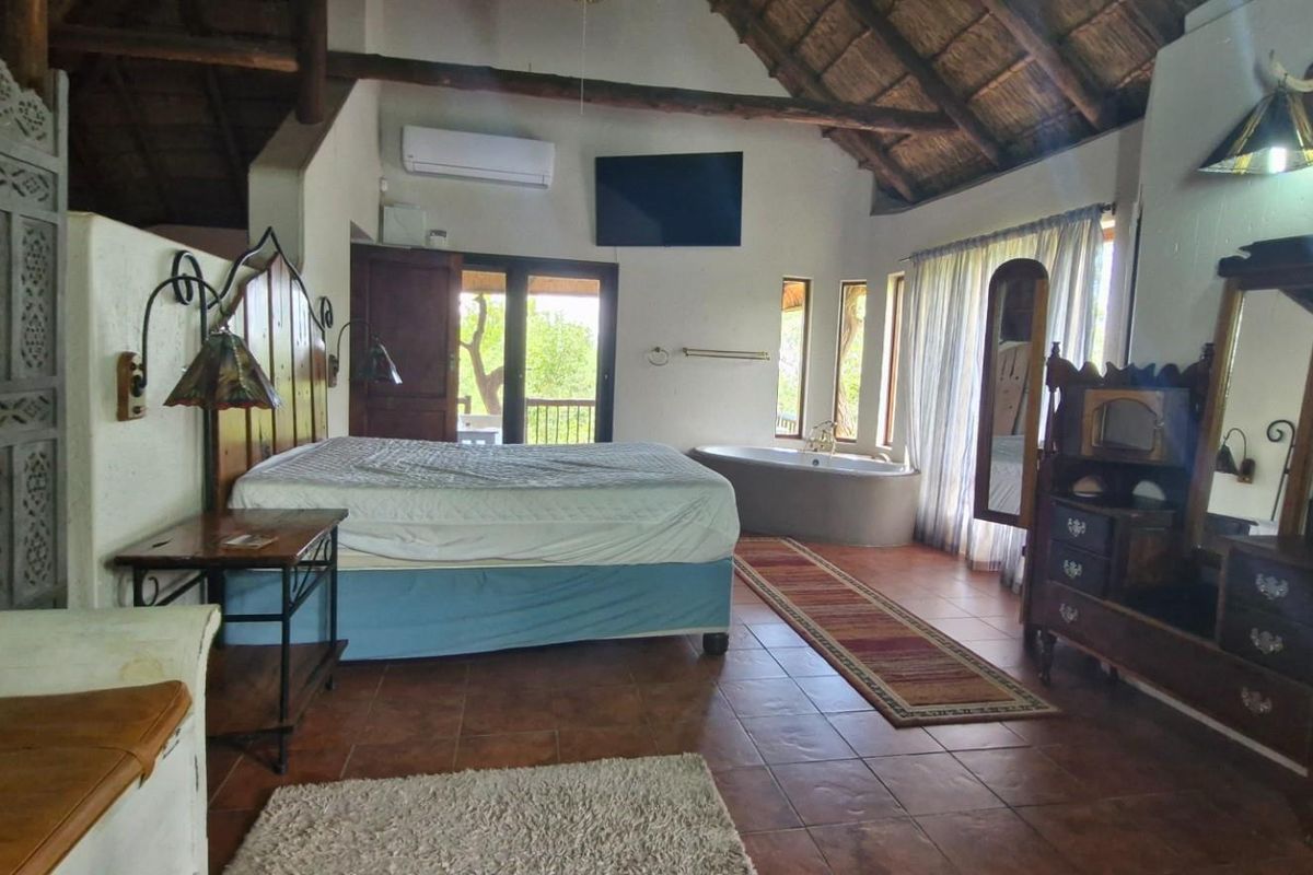 Spacious bedroom featuring a high thatched ceiling, integrated bathtub, and direct access to an outdoor balcony area.