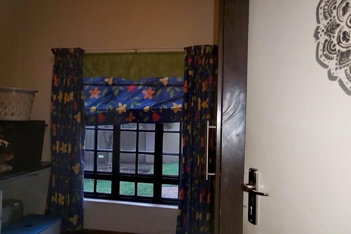 A bedroom interior featuring a dark-framed window with grid detailing, complemented by patterned curtains and a solid interior door with modern hardware.