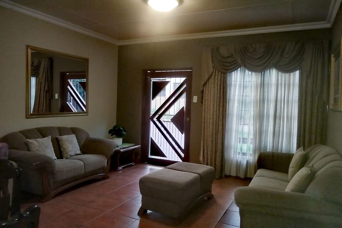 A living room featuring tiled flooring, a decorative security door, and large windows with draped curtains.
