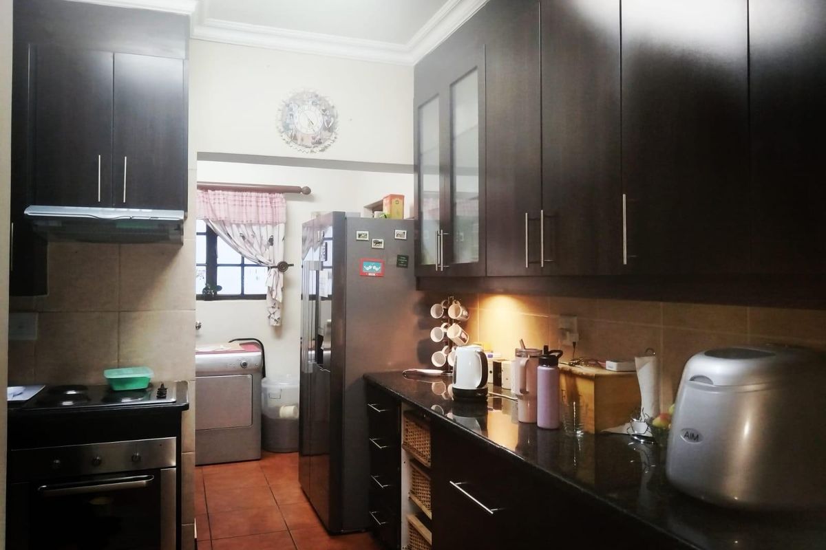 A functional kitchen featuring dark cabinetry, granite countertops, a built-in oven, and an extractor fan, with an adjacent laundry area.