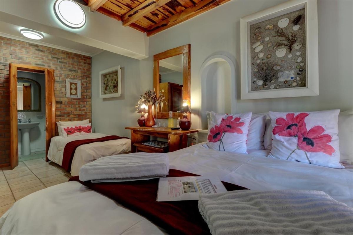 A bedroom featuring exposed brickwork, a timber-beamed ceiling, and an en-suite bathroom with a pedestal basin.