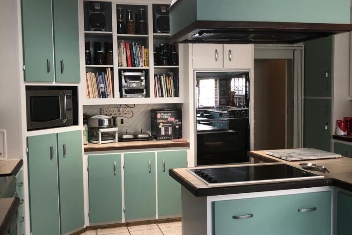 A dated kitchen featuring teal cabinetry, a central island with a built-in cooktop, a large overhead extractor fan, and tiled flooring.