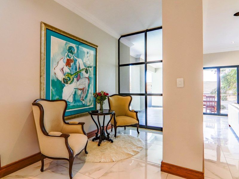 A bright, elegant hallway featuring polished porcelain tile flooring, decorative skirting, and a modern black steel-framed glass partition leading to the outdoor area.