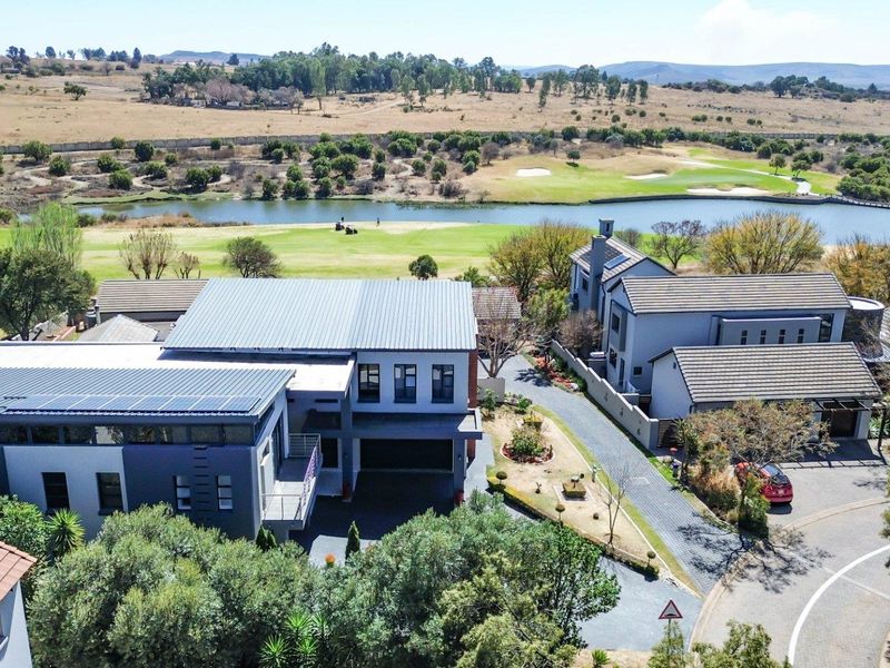 Aerial view of a modern multi-story residence featuring a metal roof with solar panels, a paved driveway, and a scenic golf course backdrop.