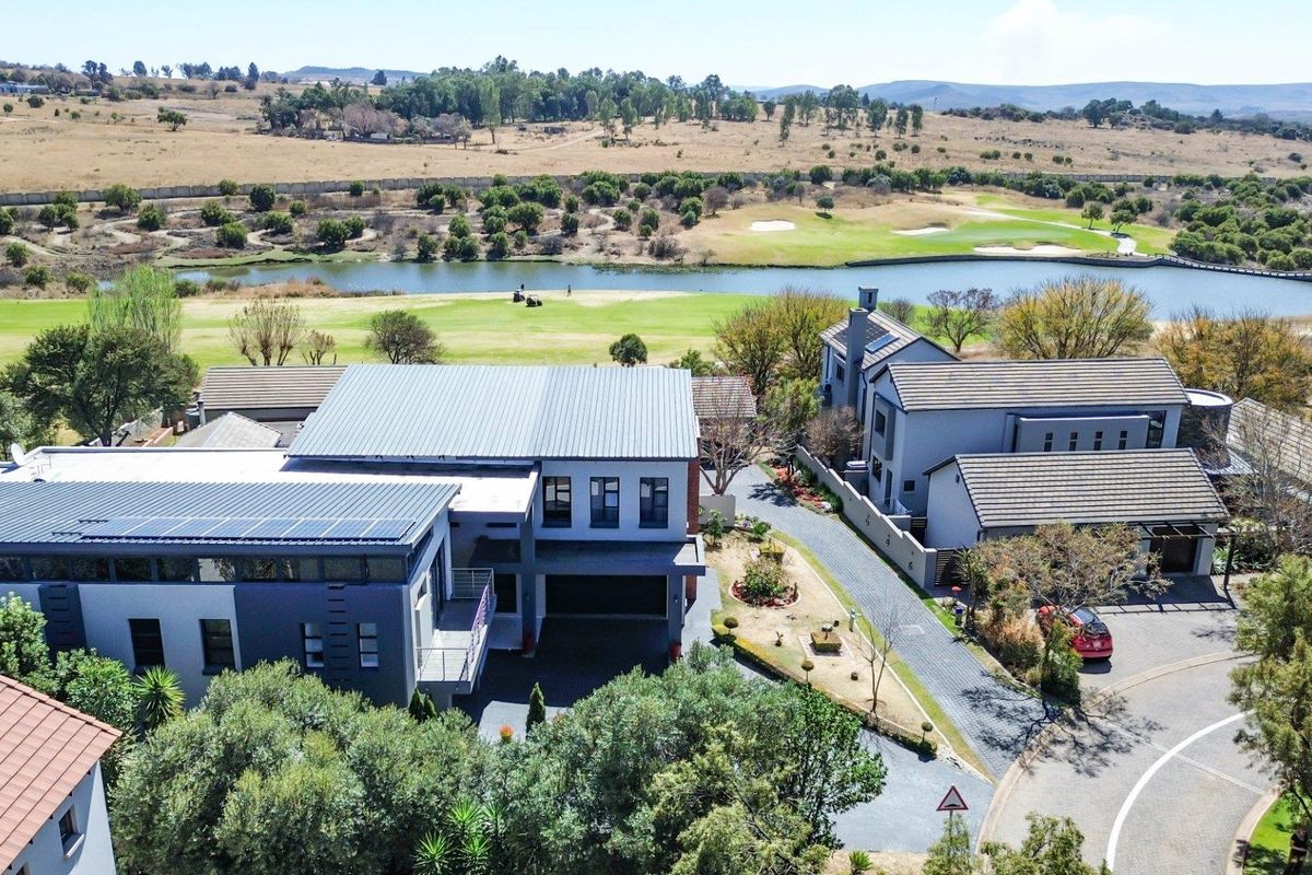 Aerial view of a modern multi-story residence featuring a metal roof with solar panels, a paved driveway, and a scenic golf course backdrop.
